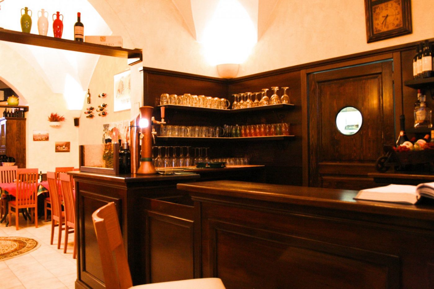 Il bancone in legno scuro del Toro Nero con la spina della birra, boccali e bicchieri allineati sulle mensole e l'orologio a muro