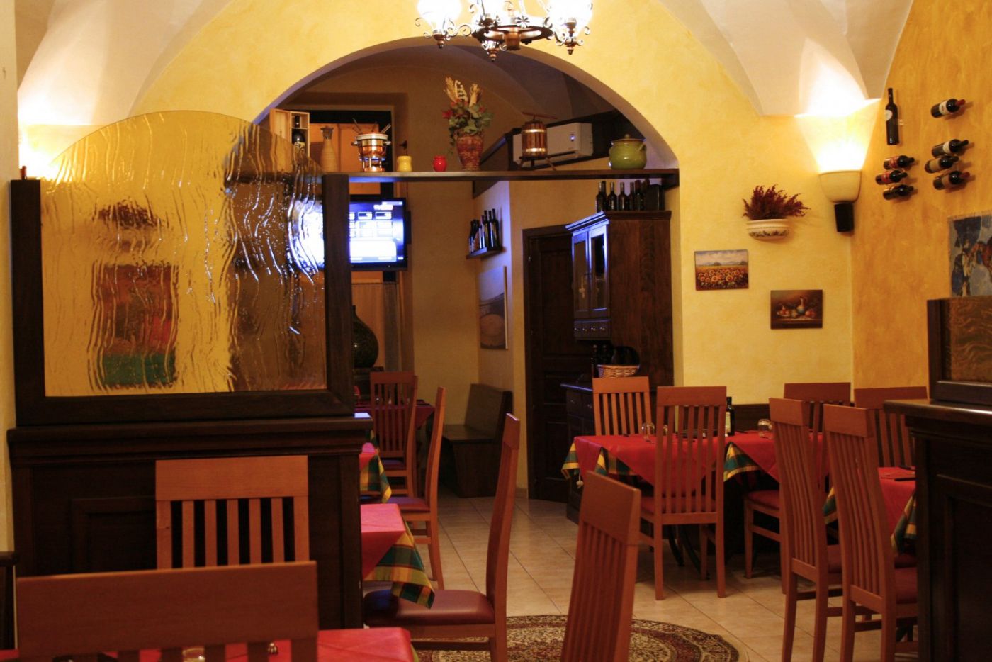 Seconda sala del Toro Nero vista attraverso un arco in muratura, con volte a crociera bianche, lampadario in ferro battuto e file di tavoli apparecchiati con tovaglie rosse